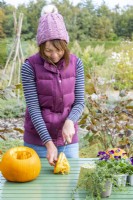 Woman using a knife to cut the pulp off of one of the pumpkin tops