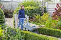Woman pushing wheelbarrow through garden