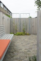 Wooden fence with climbers at the patio. Special designed wooden bench at wooden fence with orange cushions. Lighting at fence.