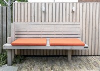 Special designed wooden bench at wooden fence with orange cushions. Lighting at fence.