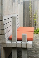Special designed wooden bench at wooden fence with orange cushions. Lighting at fence.
