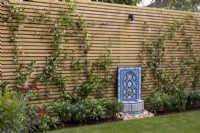 Decorative Arabic style water fountain in front of wood slatted fence with Trachelospermum jasminoides