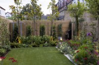 Contemporary suburban garden in London with colourful borders, artificial lawn and lighting