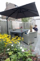 Women sat by modern table in small urban garden with Rudbeckia in foreground.