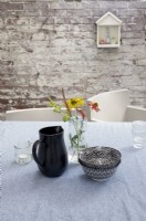 Table set with water jug, bowls and vase of flowers. Old wall brick wall beyond.