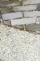 Metal edging strip separating path of brick and gravel.