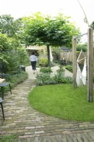 Woman walking along curved brick path in a small modern garden.