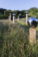 Avenue in meadow of stainless steel globes mounted on wooden pillars with surroundings reflected in the globes. July, Summer.