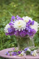 White dahlias arranged with lilac lathryrus odorata - sweet peas and scabious in glass jug on pink table