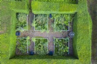 View over small formal garden contained by clipped Yew hedges; image taken with drone. Brick paths and rectangular beds contained by railings July. Summer.