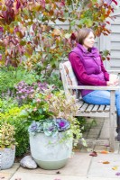 Woman sitting on a bench next to an Autumn container arrangement