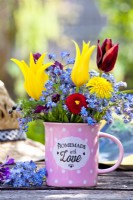 Bouquet of spring flowers in a tea cup - forget me nots, tulips, bellis and dandelion.