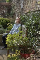 Woman sitting at the garden table surrounded by Narcissus 'Hawera', Trachelospermum jasminoides.