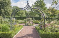 Looking through 'Gothic' arch planted with Clematis Blekitny Aniol syn. Clematis Blue Angel and scented Rosa 'Hardwell' to planter at central meeting-point of paths in contemporary walled-garden at Dumfries House. 

Lilium regale and Echinacea syn. cone-flower growing at base of arch.  Paths edged with Buxus sempervirens syn. Box. September.