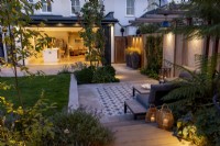 Contemporary garden at night with patio and pergola, looking towards house and kitchen