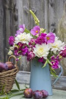 Pink and white bouquet of summer flowers in blue enamel jug - white Dahlias, pink Cosmos, Lathyrus and Scabious with basket of plums against wooden background