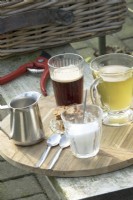 Coffee, tea, sugar and milk on wooden tray and pruning shears on wooden bench.
