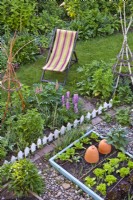 Vegetable beds, flowerbeds and lawn with a deck chair.