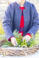 Woman using wire to secure variegated Osmanthus sprigs to the wreath
