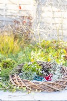 Wreath, greenery, pine cones, berries, red ribbon and snips laid out on a wooden surface