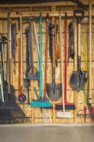 Stored assorted gardening tools on wall of garden shed - June