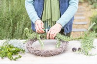 Woman using wire to secure Rosemary to the wreath