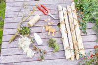 Birch sticks, various foliage, bark stars, wooden reindeer, string, glue and snips laid out on table