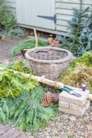 Bricks, secateurs, wire, moss, conifer branches, basket and a large birch stick laid out on the ground