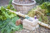 Bricks, secateurs, wire, moss, conifer branches, basket and a large birch trunk laid out on the ground