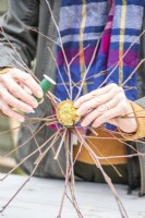 Woman wiring the painted twigs to the wooden disc