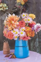 Pink and Orange flower arrangement of Dahlias and Chrysanthemums with dried fennel in blue enamel jug on table against wooden background