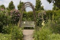 Bench seat in rose garden with an arch created from bent willow branches