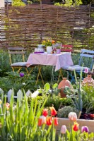 Kitchen garden in spring, table and seats with floral arrangement.