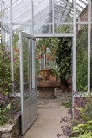 View through open door to greenhouse interior, with large potted fuchsia and other plants