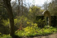 A carved stone gate surrounded by spring foliage near the water garden at Thenford Gardens and Arboretum, Thenford, Banbury, Oxfordshire, UK