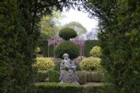 A baroque carved stone cherub statue surrouned by clipped Box hedge and Yew topiary in the sculpture garden at Thenford Gardens and Arboretum, Thenford, Banbury, Oxfordshire, UK