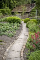 Simple brick-edged paved path leads through cottage style garden with vegetables and flowers either side