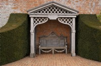 An ornate carved wood gazebo and garden bench outside the walled garden at Thenford Gardens and Arboretum, Thenford, Burford, Oxfordshire, UK