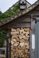 Log store with piled up logs inside shed and outdoor thermometer

