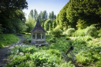 Summerhouse beside the stream edged with hostas, primulas and ferns in the bog garden at the Old Rectory, Netherbury, Dorset in May