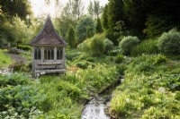 Stream runnning through a bog garden in May past a timber summerhouse at the Old Rectory, Netherbury, Dorset, the ground covered with moisture loving plants including hostas, primulas and ferns