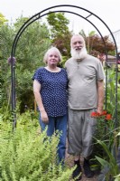 Couple standing under arch in their garden in August.