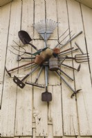 Old farm and garden tools hung on white barn wall in backyard country garden, Quebec, Canada - August