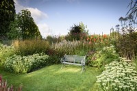 Metal bench surrounded by herbaceous perennials at Highfield Farm in August including Hylotelephium spectabile and kniphofias.