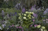 Bodmin Jail: 60 Degrees East - A Garden Between Continents. Designers: Ekaterina Zasukhina and Carly Kershaw. Rocks, waterfall and plants including Anemone x hybrida, Hydrangea, Astrantia major 'Star of Billion', Thalictrum 'Hewitts Double' and Veronica longifolia. Chelsea Flower Show 2021.