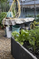 A large empty cable reel has been upcycled to make a potting surface and storage place for tubs and buckets in the middle of a vegetable garden with raised beds made from upcycled paving slabs. Derrydown, an NGS garden. July. Summer. 