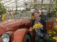 Jonathan Moseley the floral designer next to a Morgan car in Malvern and holding a yellow display of Orchid flowers.