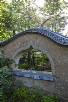 Cob wall structure in garden, with arched window 'peephole'