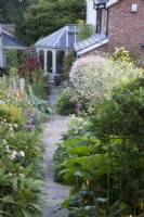 Looking down a garden path and perennial borders towards a house.