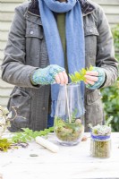Woman using a small stick to position fern fronds inside a glass container